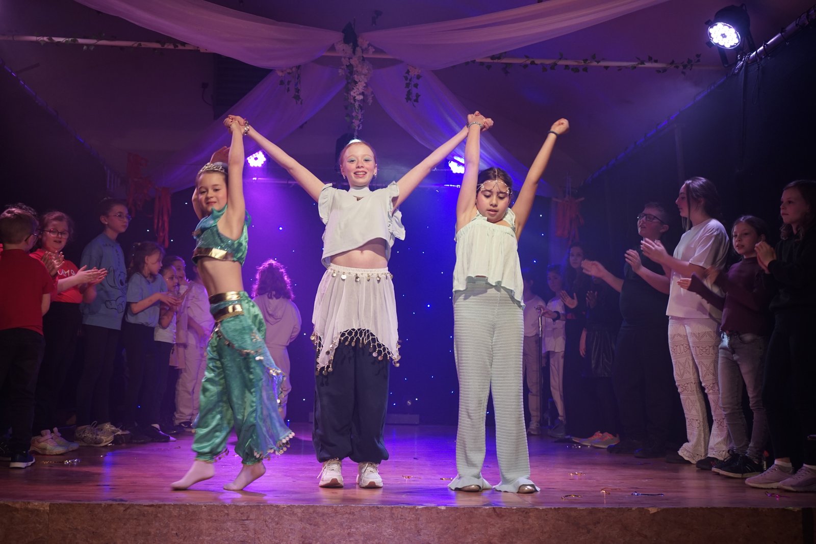 Enfants triomphants sur scène, bras levés sous les projecteurs